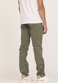 Pantalon en coton vert olive à coupe slim, doté de poches latérales et de détails de couture subtils. Associé à des baskets blanches et un t-shirt blanc uni.