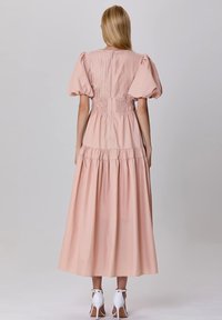 Robe longue rose clair avec des manches bouffantes, une taille smockée et une jupe à volants. Texture lisse avec de subtils plis à l'arrière.