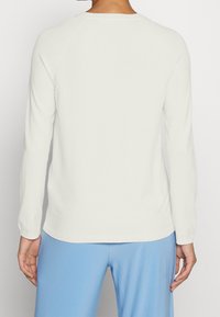 Vit långärmad stickad topp med rund halsringning och ribbad manschett, med en slät yta och en något avslappnad passform.