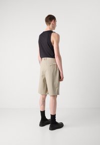 Pantalones cortos beige de corte regular, fabricados en una mezcla de algodón ligera, con un bolsillo trasero. Combinados con una camiseta sin mangas negra ajustada y calzado negro.