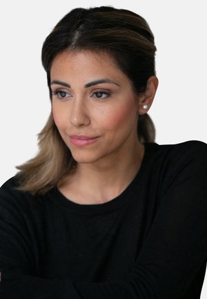 Porträt einer Frau mit schulterlangem, braunem Haar, die ein schwarzes Langarmshirt trägt. Sie hat Perlenohrringe und ein neutrales Make-up.