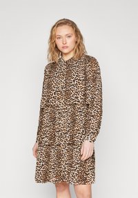 Abito a stampa leopardata con maniche lunghe, colletto abbottonato, strati sovrapposti, tessuto leggero, caratterizzato da macchie marroni e nere su uno sfondo beige.