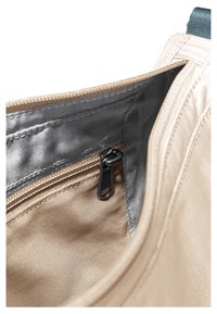 Close-up van de binnenkant van een beige tas met een zwart ritstrekkertje en zilverkleurige voering in het binnenvak.