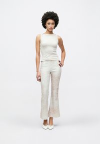 Canottiera beige chiaro con una forma aderente e spalline larghe, abbinata a pantaloni a zampa d'elefante con motivo nei toni crema e beige chiaro.