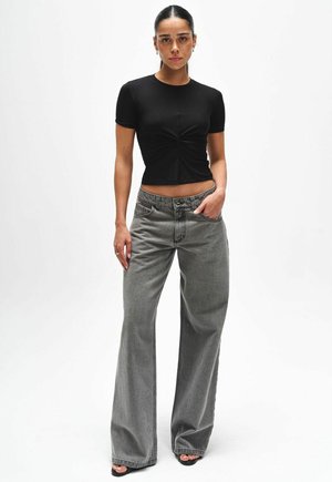 Black cropped t-shirt with a twisted front design, paired with high-waisted, loose-fitting gray jeans. Flat black sandals complete the look.