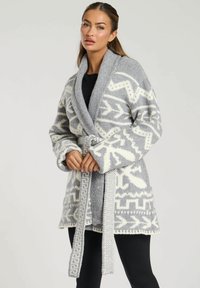 Grå stickad cardigan med ett vitt geometriskt mönster, bred sjalkrage och matchande bälte. Långa, lösa ärmar och mjuk textur.