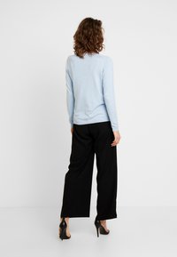 Maglione azzurro chiaro con maniche lunghe e scollo tondo, abbinato a pantaloni neri a gamba larga e scarpe nere con tacco alto.