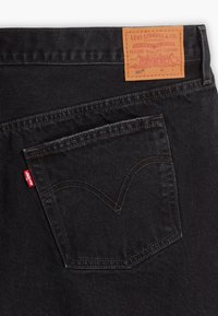 Poche arrière d'un jean Levi's noir avec l'étiquette rouge emblématique et une étiquette en cuir beige affichant la marque et les détails de la taille.
