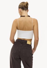 Top court blanc avec bretelles fines, associé à un pantalon taille haute marron foncé avec poches arrière et une étiquette en cuir.