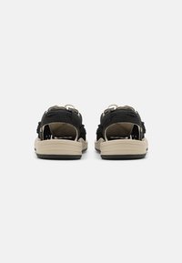 Sorte sandaler med åben bag, struktureret overmateriale, beige sål og dobbelte runde spænde detaljer for justerbar pasform.
