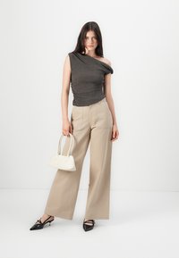 One-shoulder, dark gray top with textured fabric, paired with light beige wide-leg trousers. Accessories include a small white handbag and black pointed shoes.
