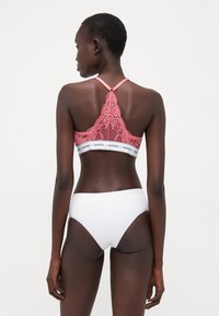 Bralette in pizzo rosa con retro a scallop, dotato di un cinturino con logo bianco. Abbinato a slip bianchi a coste, con texture liscia e design aderente.