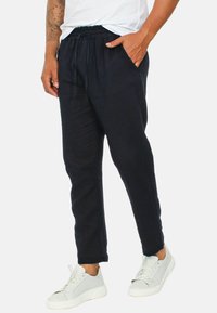 Pantaloni jogger blu navy con vita elastica, tasche laterali e vestibilità comoda, abbinati a sneakers bianche.