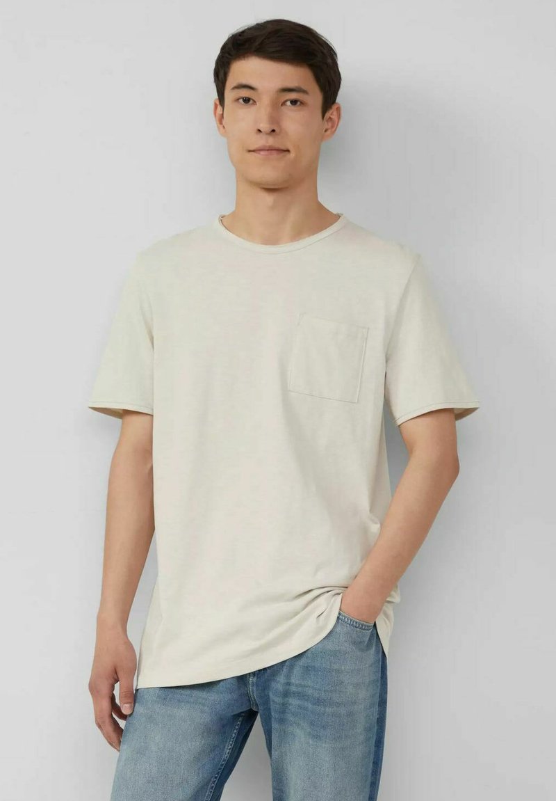 Hellbeige T-Shirt aus weichem Stoff, mit kurzen Ärmeln, rundem Ausschnitt und einer kleinen aufgesetzten Tasche auf der linken Brust.