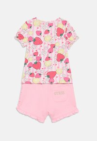 Σετ δύο τεμαχίων που περιλαμβάνει ένα ροζ τοπ με κοντά μανίκια και σχέδιο φρούτων, και ροζ σορτς με βολάν στα τελειώματα και κεντημένο το "GUESS" στην τσέπη.