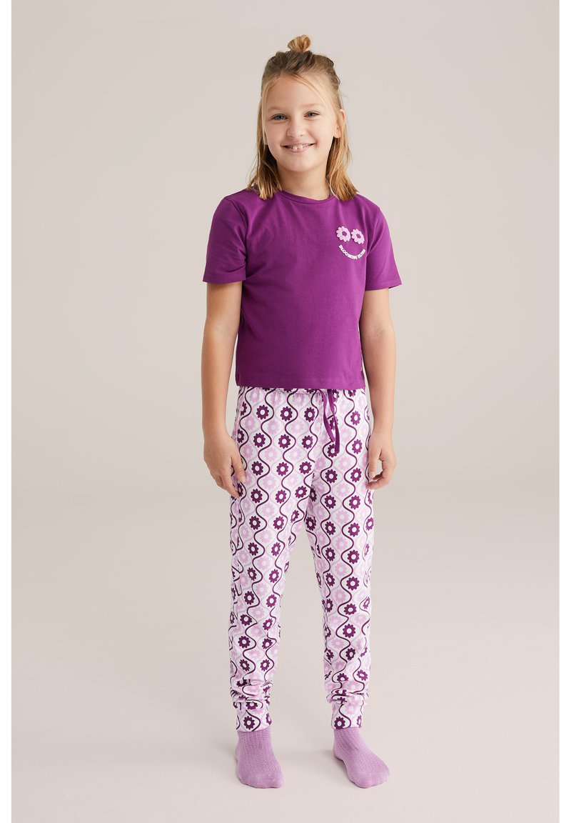 Camisa corta de manga púrpura con un gráfico de flores, combinada con pantalones de pijama blancos con un patrón de flores púrpuras y rosas.