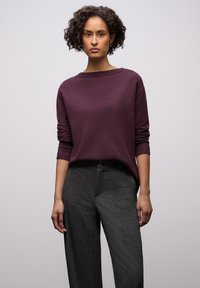 Paarse trui gemaakt van zachte stof met een ronde hals en lange mouwen, gecombineerd met grijze, loszittende broek. Eenvoudig ontwerp met minimale textuur.