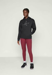 Svart huvtröja med vitt tryck på bröstet, kombinerad med vinröda leggings och svarta sneakers, med vita detaljer och en slät textur.