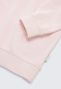 Sudadera rosa claro con puños y dobladillo acanalados, textura suave, costuras sutiles y una pequeña etiqueta en el lateral con la marca.