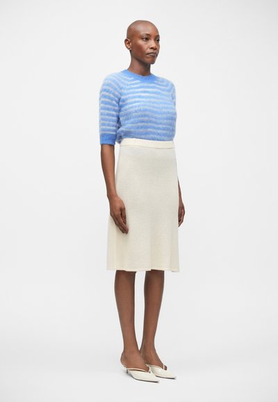 Pull à manches courtes rayé bleu, jupe évasée crème et mules blanches à bout ouvert. Textures douces, coupe décontractée et lignes épurées.