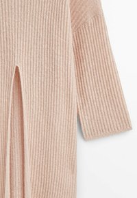 Tissu tricoté côtelé rose clair avec une fente verticale à l'avant et une manche trois-quarts, visible sur un fond blanc.