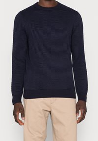 Marinblå texturerad tröja med rundad hals, ribbade ärmslut och nederkant, med ett upphöjt mönster och tillverkad av ett mjukt stickat tyg.