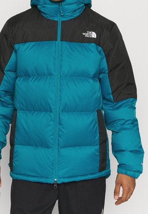 Pikowana kurtka w kolorze morskim i czarnym z pełnym zamkiem, z przeszywanym wzorem i wysokim kołnierzem. Logo na górnej lewej stronie. Tkanina o teksturowanej strukturze.