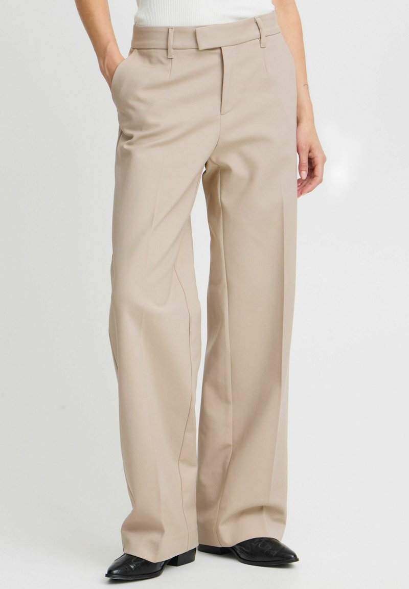 Pantalons larges beiges en tissu lisse, dotés de passants de ceinture, de deux poches latérales et d'un pli sur le devant.