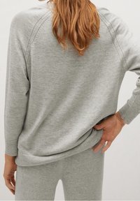 Jasnoszary sweter o luźnym kroju i ściągaczach. Posiada prosty design z przeszyciami wzdłóż ramion i u dołu.