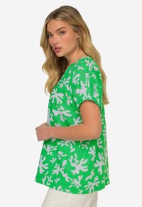 Top verde a maniche corte con un motivo astratto bianco, realizzato in tessuto leggero, con una vestibilità rilassata e scollatura a girocollo.