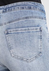 Ljusblå denimjeans med en bakficka. Karakteriseras av en sydd kontur, subtila blekningar och en jämn textur.