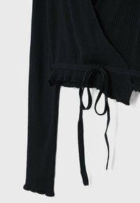 Black ribbed wrap top with long sleeves, featuring a tie closure and ruffled hem. Made from a textured, stretchy material.