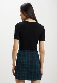 Top corto a maniche corte a coste nere con scollatura tonda abbinato a una gonna a tubino a quadri in tonalità verde scuro e blu navy.