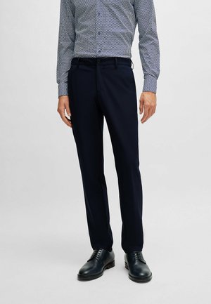 Pantaloni navy su misura con una texture liscia, caratterizzati da gamba dritta e tasche frontali. Abbinati a una camicia a righe e scarpe nere.