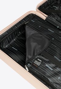 Open beige koffer met zwarte binnenvoering met vliegtuigpatronen, met ritsvakken en een merklabel binnenin.