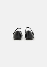 Zapatos de cuero negros con un tacón bajo, dos correas ajustables y una textura suave y mate. Diseño de punta redondeada, estilo simple y clásico.