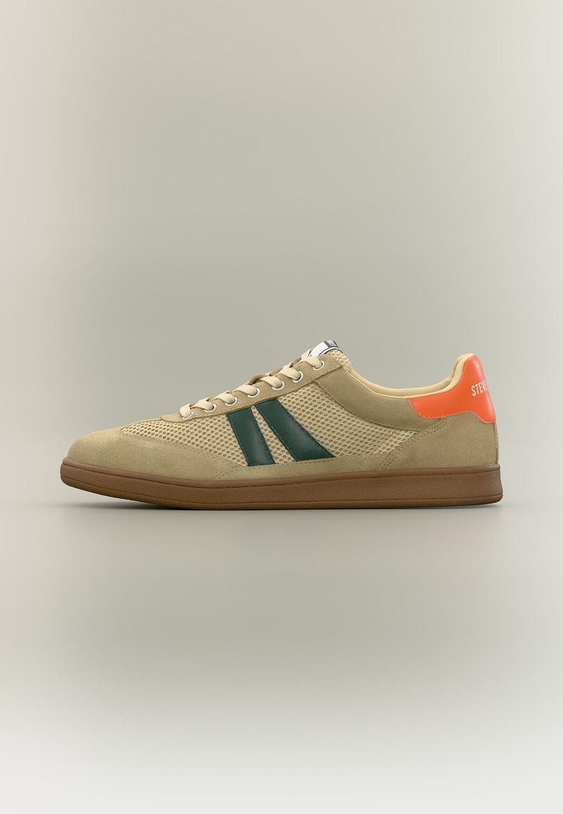 Baskets basses beiges avec côtés en maille, bandes latérales vert foncé, semelle marron et languette de talon orange avec texte blanc.