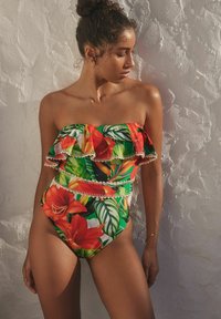 Mouwloze eenheidsswimsuit met gelaagde ruffles, met een tropisch bloemenpatroon in levendig rood, groen en geel, afgewerkt met een witte bies.