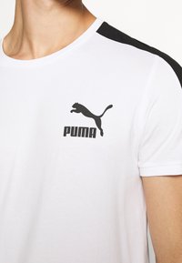 Vit kortärmad t-shirt med svarta axel-accenter, med en svart Puma-logotyp på bröstet. Tillverkad av ett mjukt tyg.