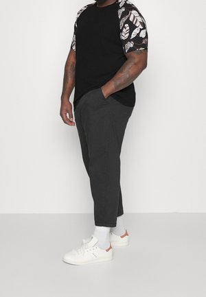 T-shirt noir avec des manches courtes à motifs présentant des designs de feuilles blanches, associé à un pantalon gris décontracté et des baskets blanches avec des accents.