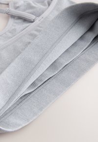 Reggiseno sportivo grigio con morbida texture a coste, spalline regolabili e bordi lisci. Il tessuto è elastico e leggero per garantire comfort.