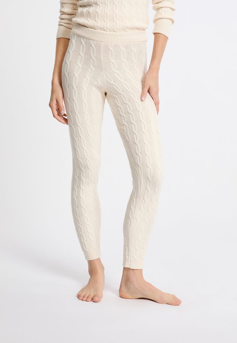 Crème kabelgebreide leggings met een textuurpatroon, taps toelopende benen en een brede tailleband, gestyled met blote voeten.