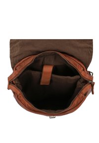 Sac à dos en cuir marron avec une fermeture éclair ouverte révélant un intérieur vide et un rabat au-dessus de l'ouverture.