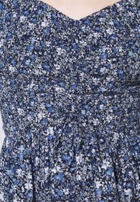 Květinové šaty s přiléhavým korzetem a rozšířenou sukňou. Tmavě modré pozadí s bílými a světle modrými květinovými vzory. Texturovaná tkanina, nařasený detail.