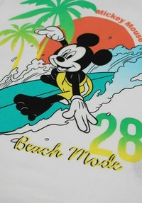 T-shirt blanc avec un graphique coloré d'un personnage de dessin animé faisant du surf, des palmiers, le texte "Beach Mode" et le numéro "28" en dégradé de vert.