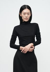 Čierny rolák s dlhými rukávmi z jemného elastického materiálu s priliehavým strihom a rebrovanými manžetami. Hladká textúra, minimálne detaily.