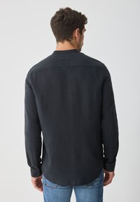 Schwarzes Langarmhemd mit weicher Textur, mit abgerundetem Saum, geknöpften Manschetten und klassischem Kragen, kombiniert mit blauen Jeans.