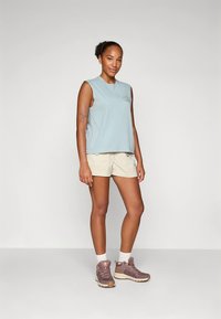 Gaiši zils piedurkņu tops, bēšas šorti, violetas pārgājienu kurpes, baltas potītes zeķes. Ikdienišķa āra apģērba komplekts ar ērtu piegriezumu un minimālu logotipu.