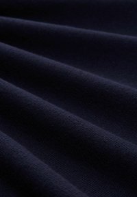 Dunkelblauter Stoff mit sanften Falten und einer glatten, fein gestrickten Textur, die aus der Nähe gezeigt wird.