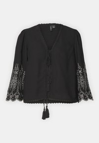 Blouse noire avec des manches larges brodées et un col en V. Dotée d'une fermeture à nouer avec des pompons et des bords festonnés. Motifs floraux détaillés en blanc.